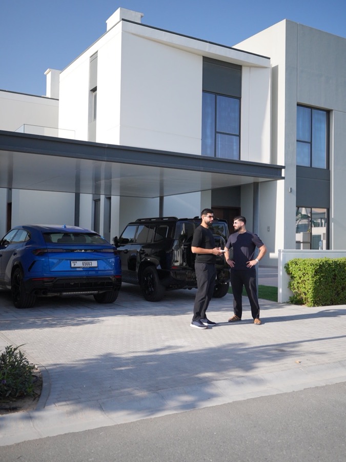 Faruk Ilkhan talking outside a house, next to two cars